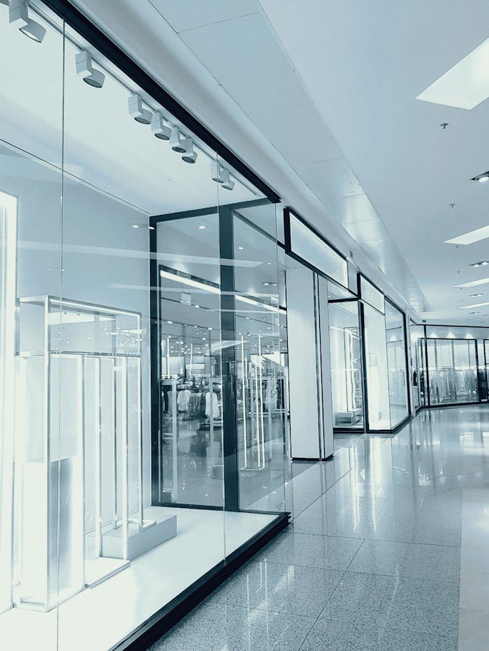 Bright and empty shopping mall corridor with glass display walls and reflections.